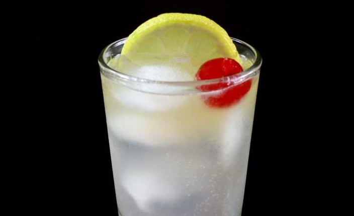 Tom Collins servido en vaso alto con hielo, rodaja de limón y cereza
