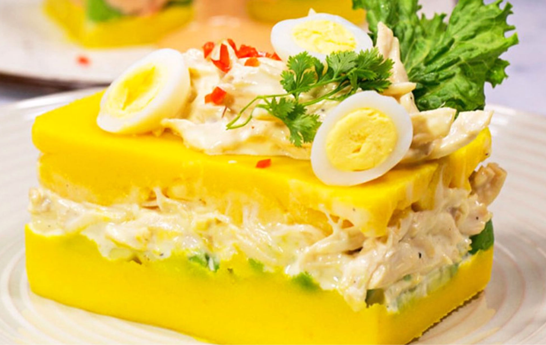 Causa limeña peruana: capas de papa amarilla con ají amarillo, relleno de pollo y palta, decorada con huevo y aceitunas