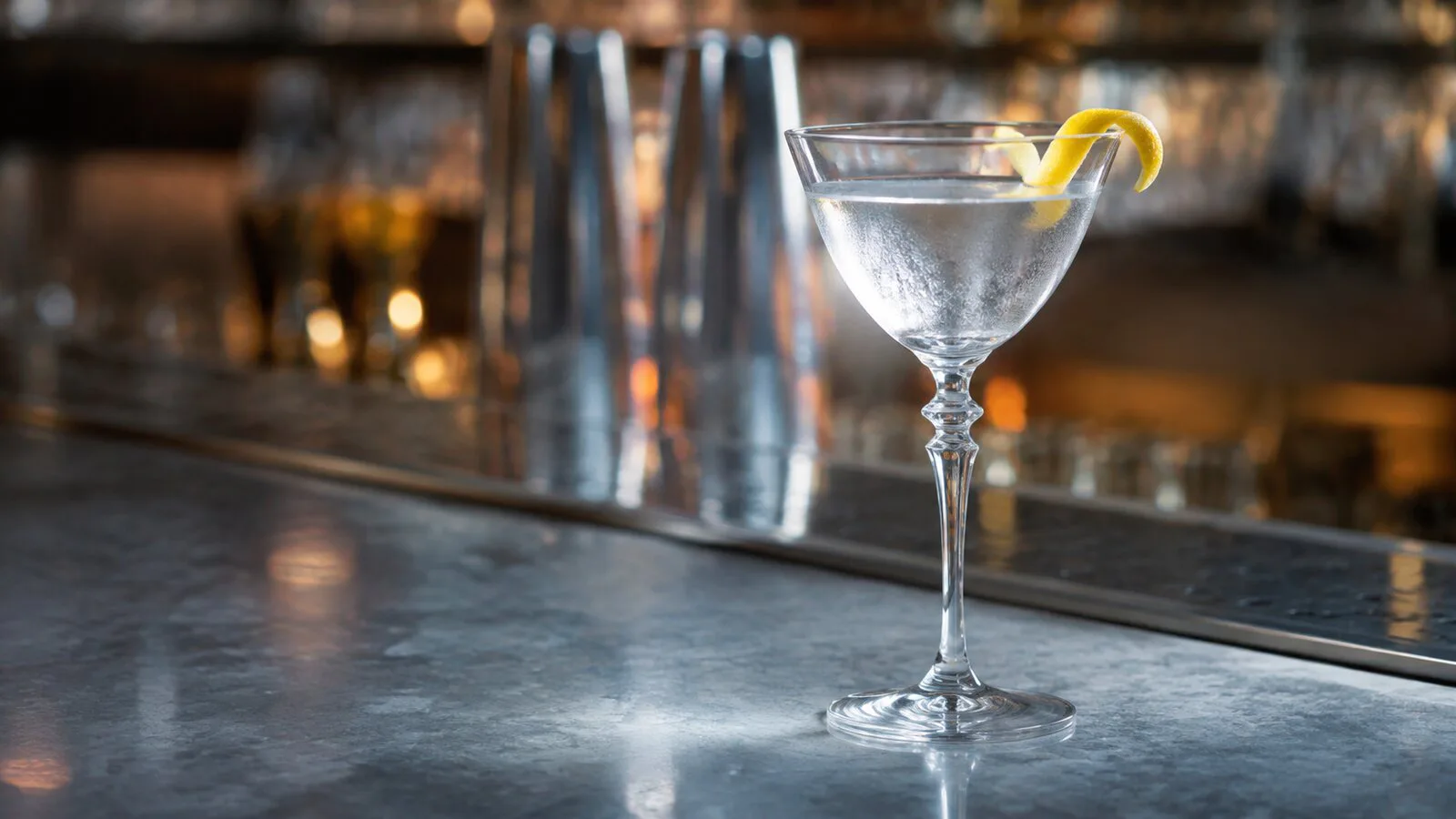 Dry Martini cristalino servido muy frío en una copa con piel de limón