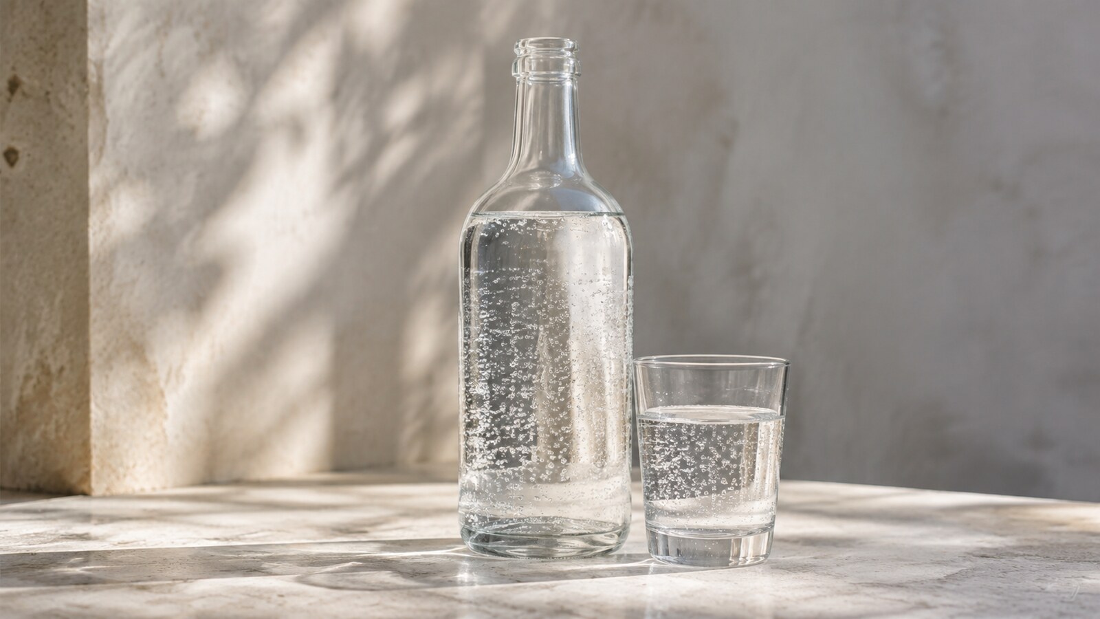Agua con gas en una botella y un vaso con burbujas finas
